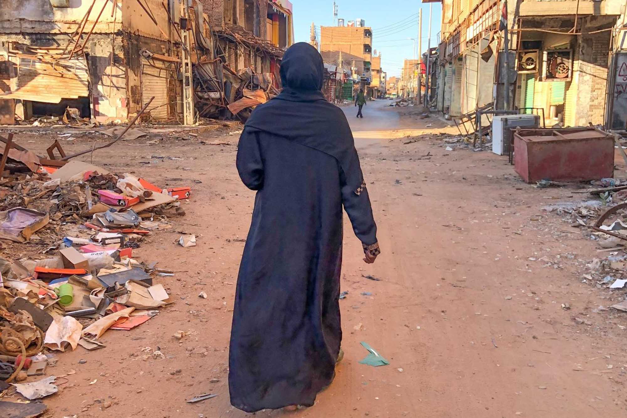 A woman walks along a desolate, war-torn urban street.
