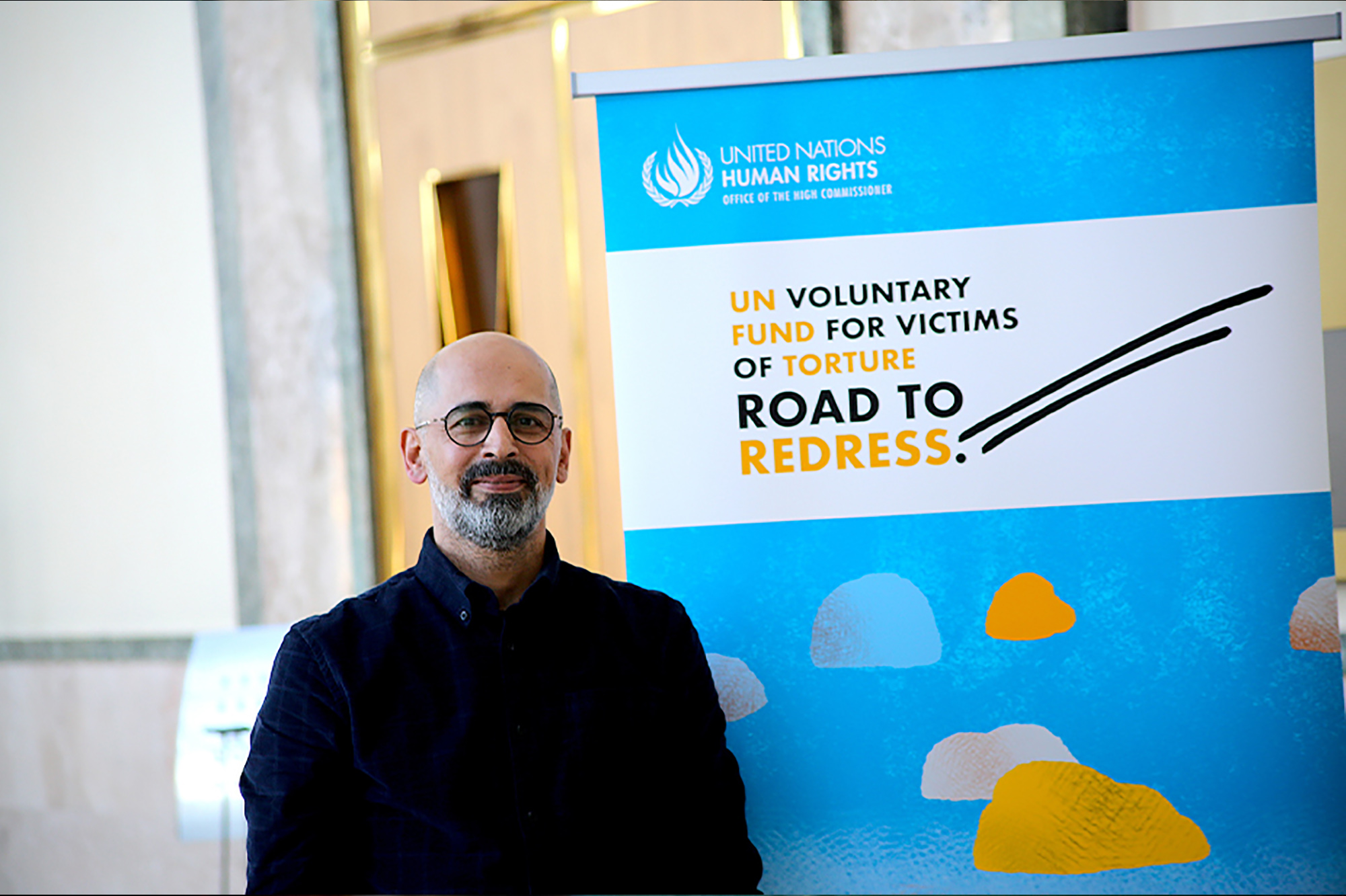 A survivor of torture stands next to a poster promoting the United Nations Voluntary Fund for Victims of Torture.