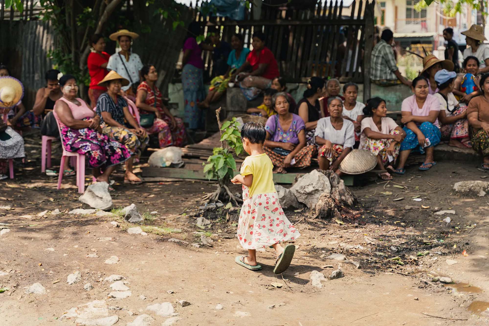 A child walking across a group of individuals in a rural outdoor setting.
