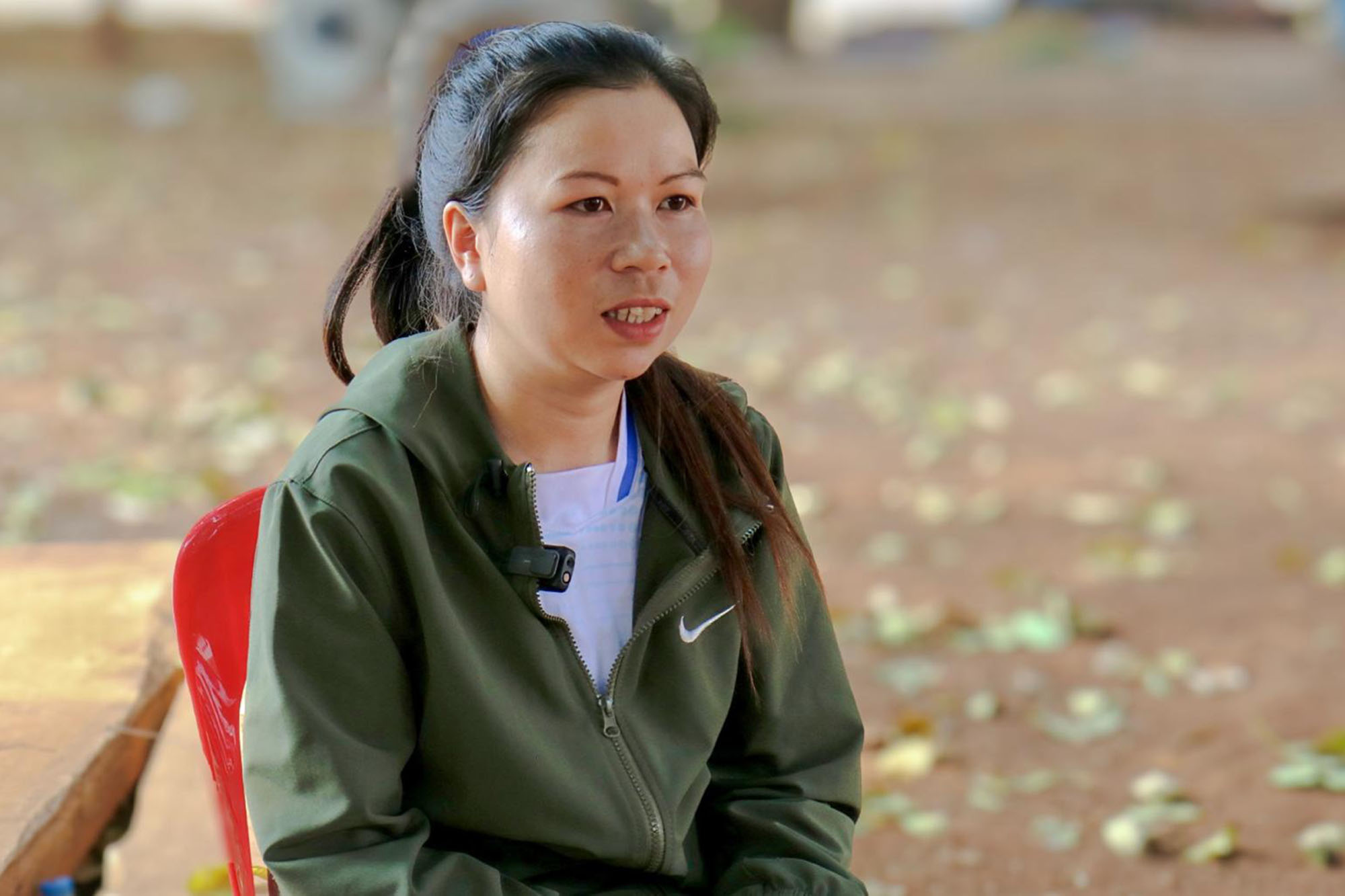 A woman seated on a bright red plastic chair outdoor.