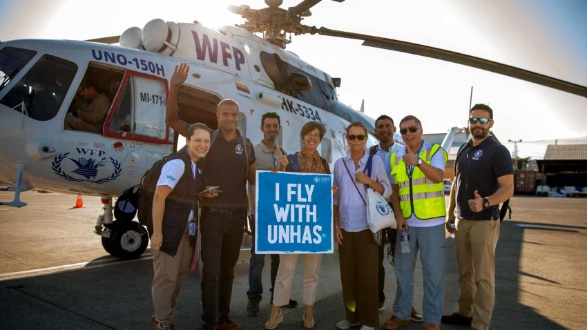 group photo in front of a helicopter while holding a poster saying I fly with UNHAS
