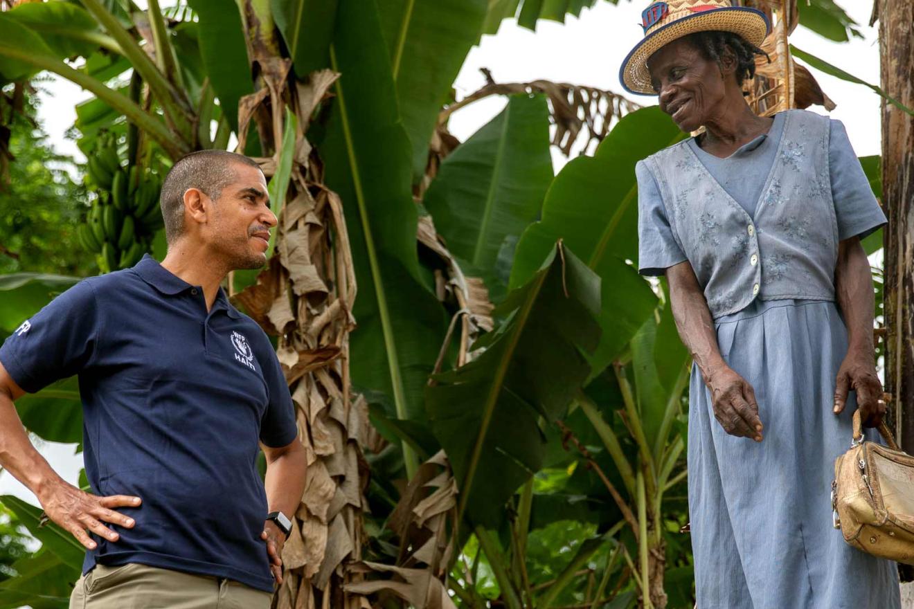 Jean-Martin is in the outdoors and facing a woman who is dressed up with a straw hat