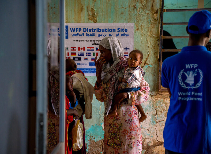 A woman holding a baby is waiting at a WFP distribution center