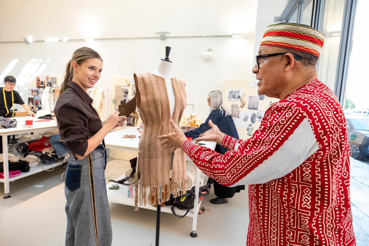 Man in African garb interacting with young fashion student.