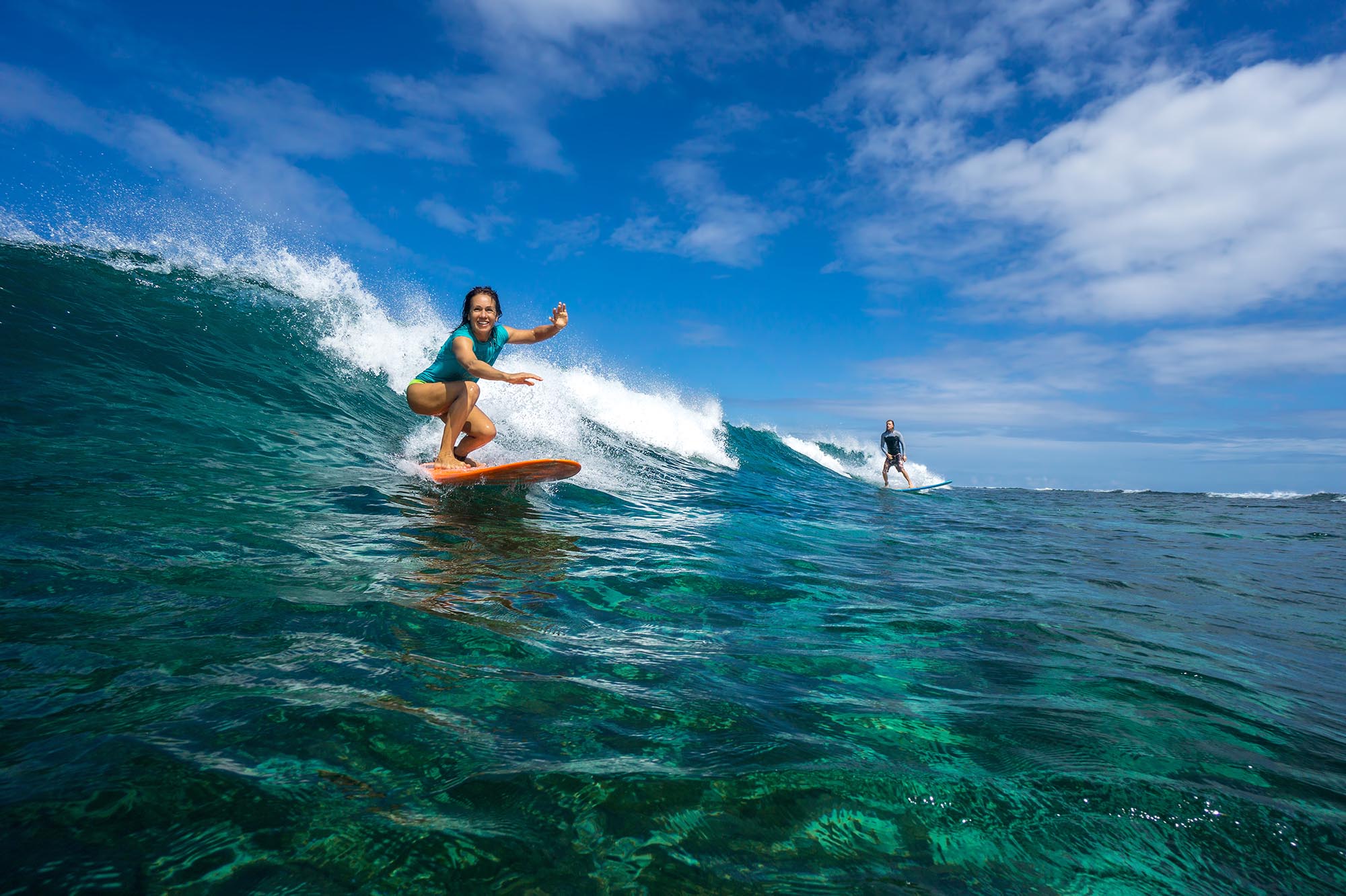 Two young surfers riding massive, crystal-clear waves.