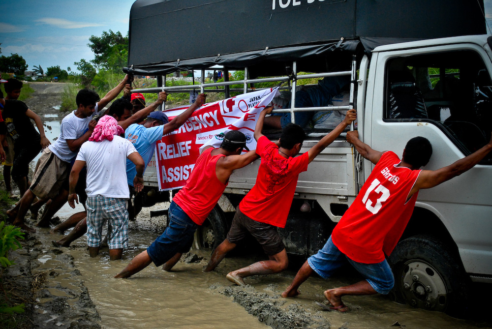 A group of volunteers trying to dislodge a truck stuck in mud.