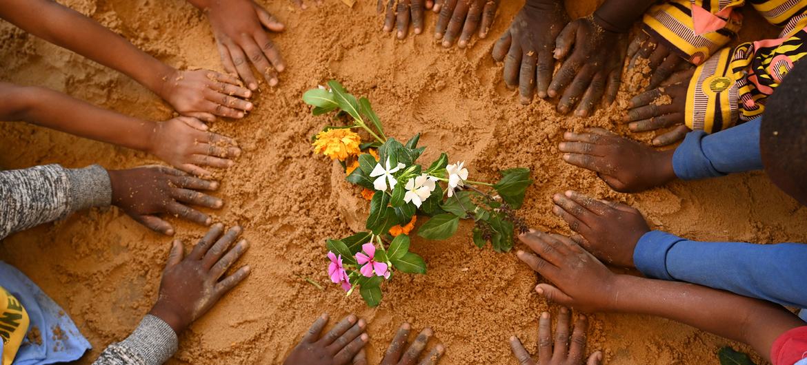 children's hands on earth around a flower