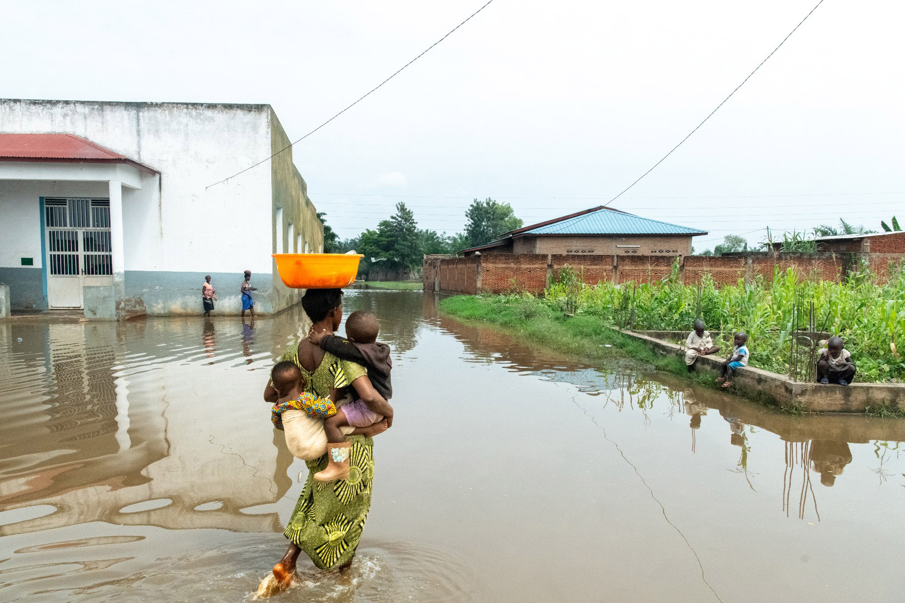 A woman crossing river carrying two children.