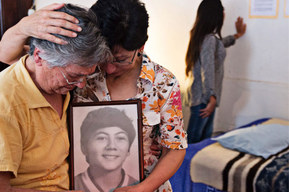 two women holding photo of teenaged boy