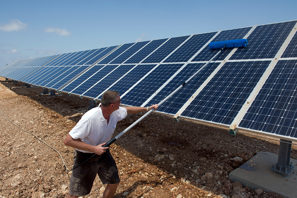A solar farmer cleans a row of solar panels.