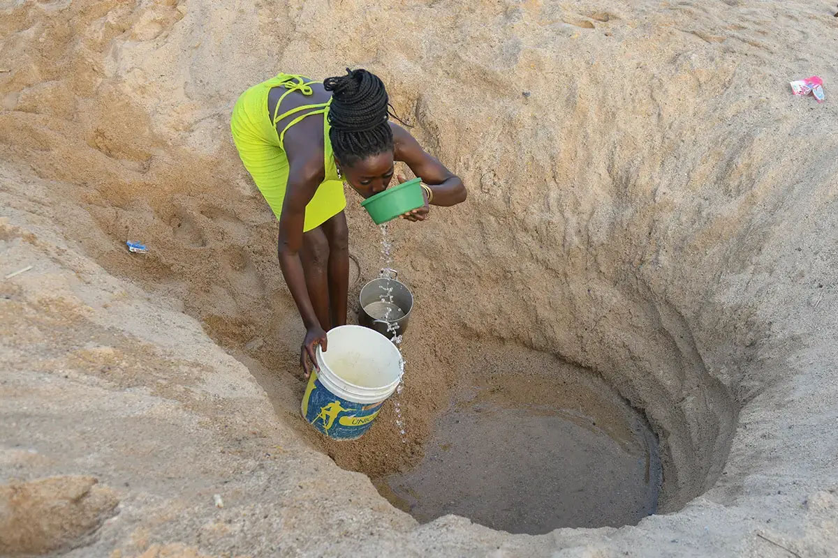 woman collecting water at bottom of borehole