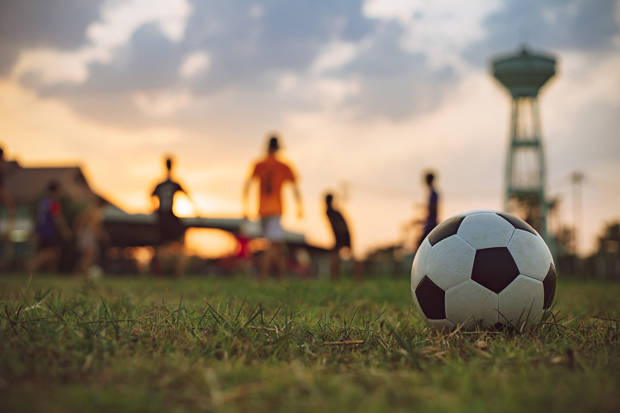 Kids playing soccer at sunset with a football in the foreground.