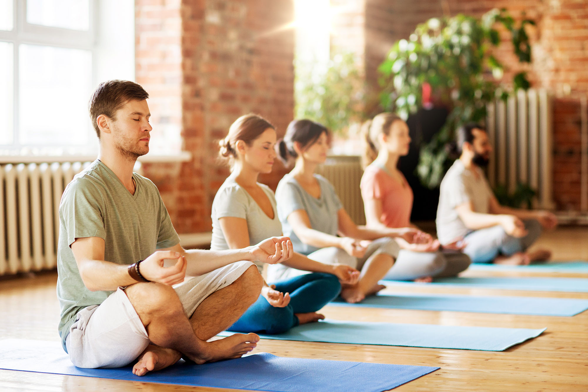 A group of people are meditating in the lotus position in a studio.